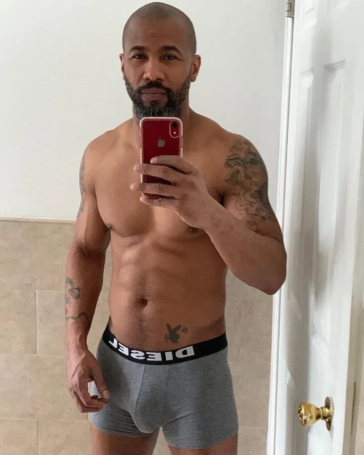 Homme torse nu, barbe fournie, sous-vêtement gris Diesel, tatouages sur les bras, prenant un selfie dans un miroir.
