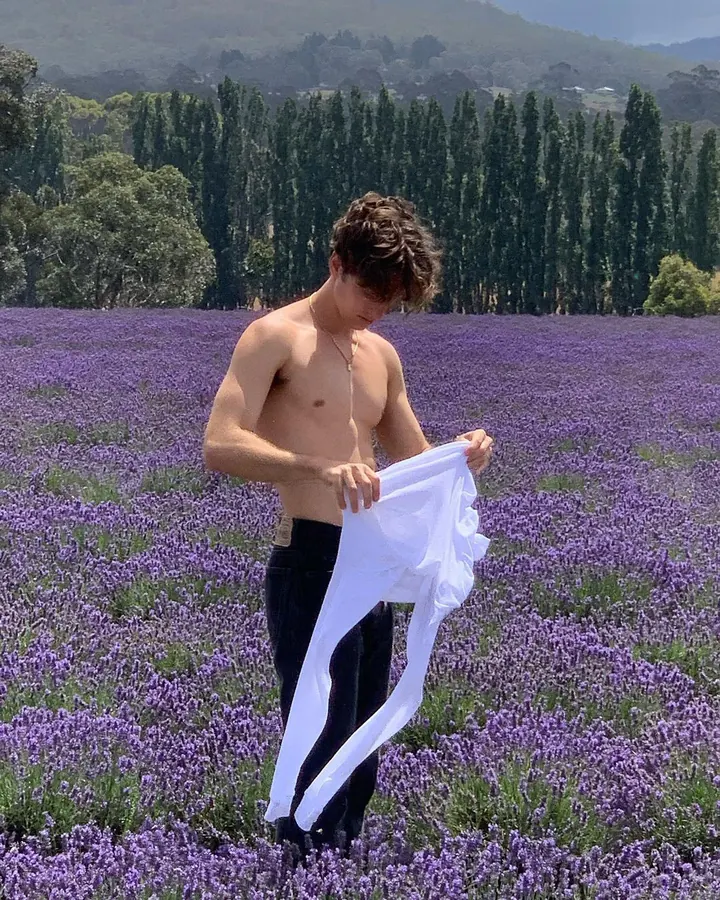Homme torse nu, en sous-vêtements, debout près d'une fenêtre, regardant vers l'appareil photo, dans une ambiance naturelle et douce.
