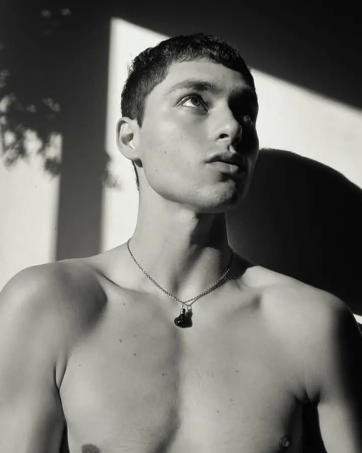 Homme torse nu, en sous-vêtements, debout près d'une fenêtre, regardant vers l'appareil photo, dans une ambiance naturelle et douce.