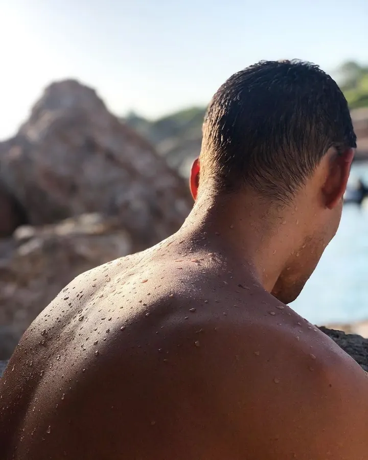 Homme torse nu, en sous-vêtements, debout près d'une fenêtre, regardant vers l'appareil photo, dans une ambiance naturelle et douce.