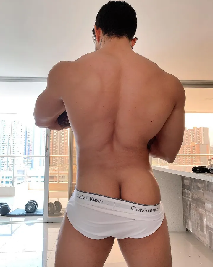 Dos musclé d’un homme en sous-vêtements blancs Calvin Klein, vue de dos, devant une fenêtre avec vue sur des immeubles