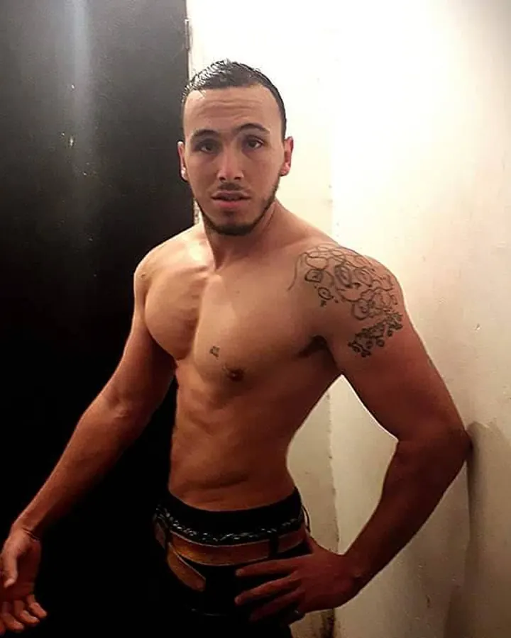 Homme torse nu, en sous-vêtements, regard intense contre un fond gris.