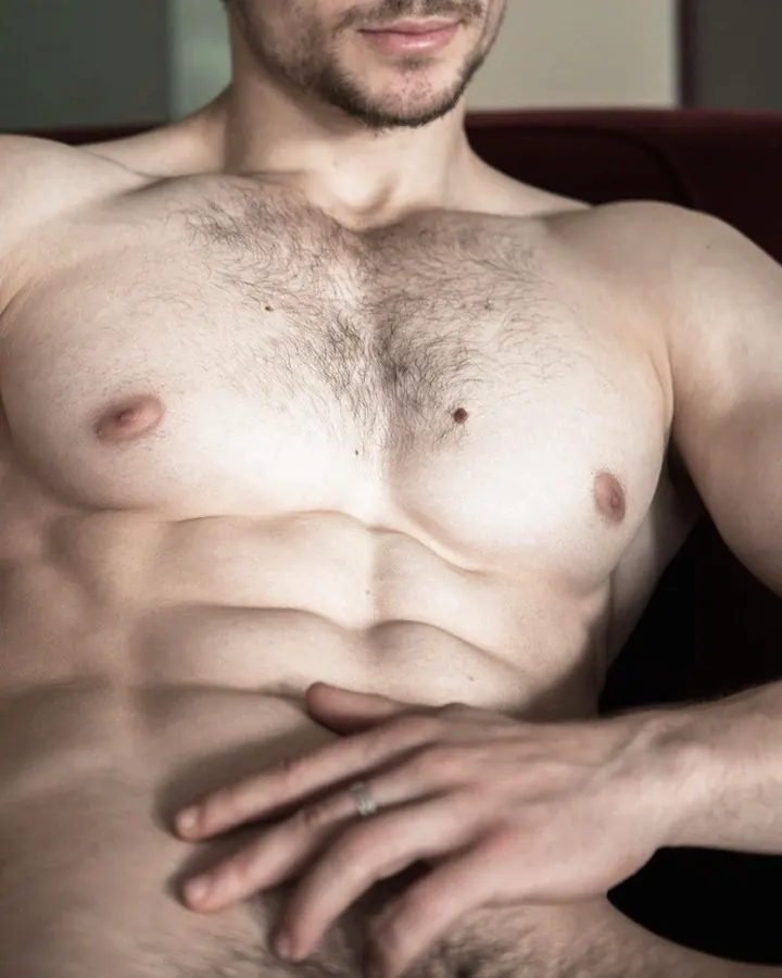 Homme torse nu, en sous-vêtements, regard intense contre un fond gris.