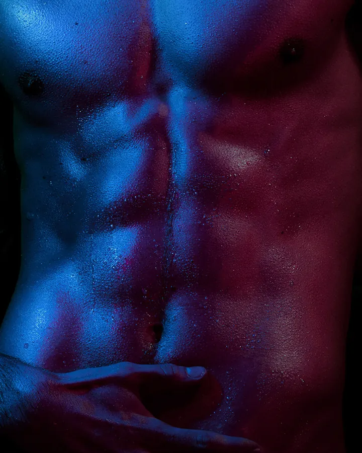 Homme torse nu, en sous-vêtements, regard intense contre un fond gris.